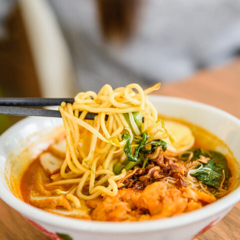 Hand with Chinese chopsticks eating noodle, a famous Malaysia prawn noodle cerry soup.